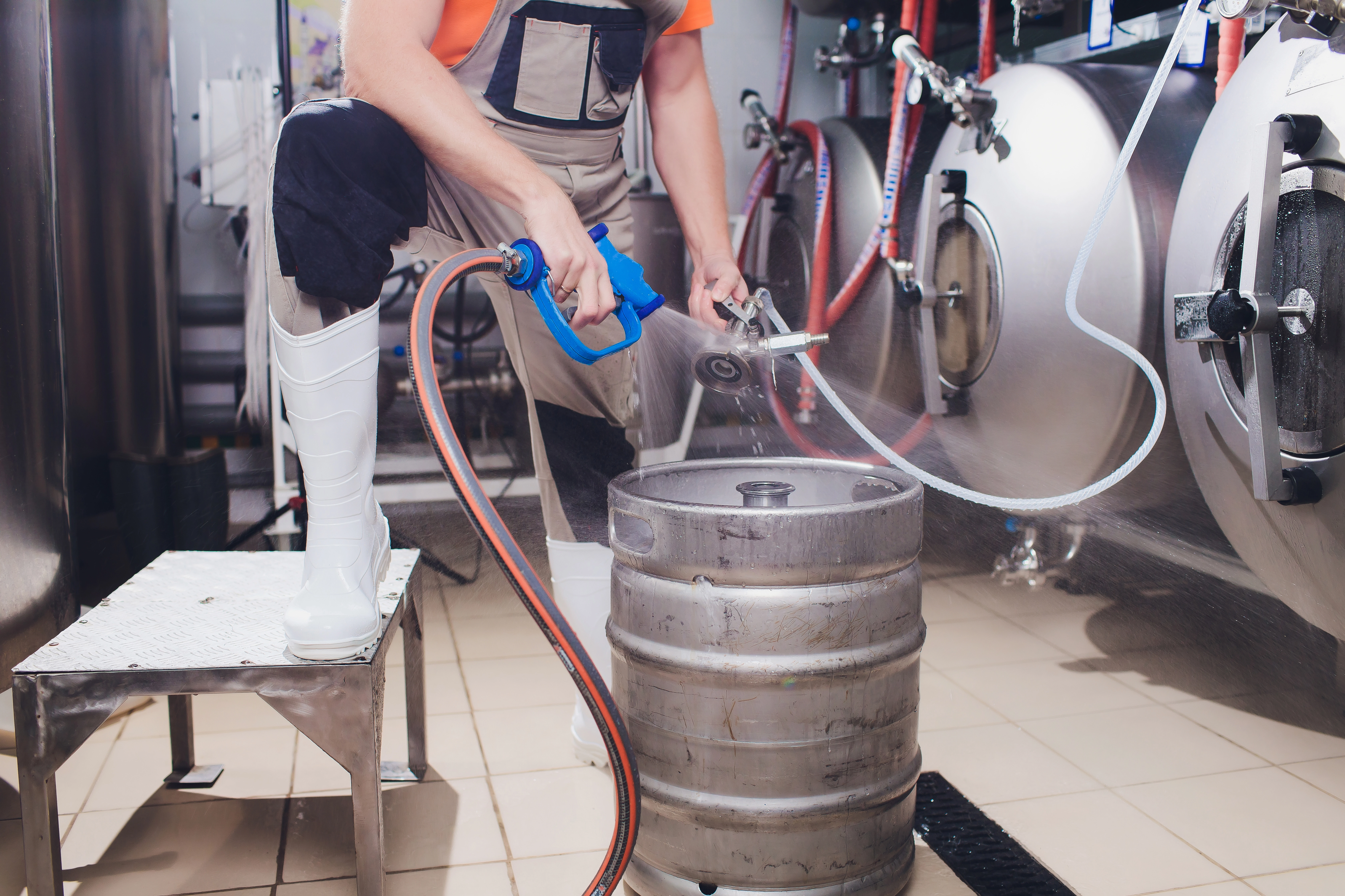 worker pressure washing a corny keg 
